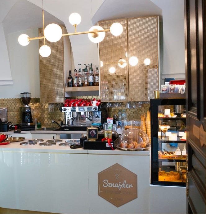 Interieur des Cafés Sznajder — goldene Bar, Espressomaschine und Kuchenvitrine